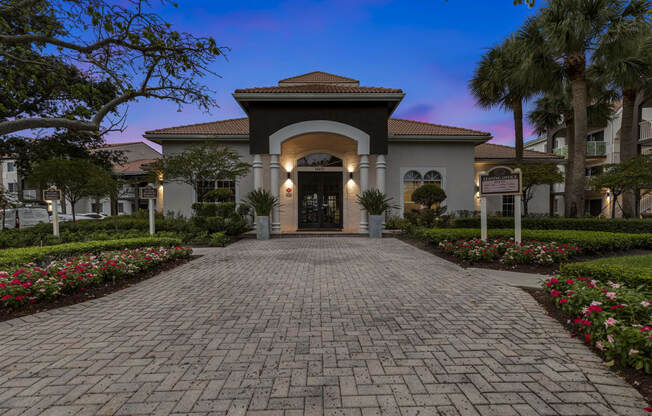 the front entrance of a villa with a brick walkway and palm trees