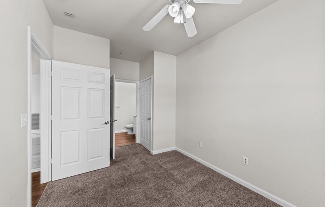 an empty bedroom with a ceiling fan and a door to a bathroom