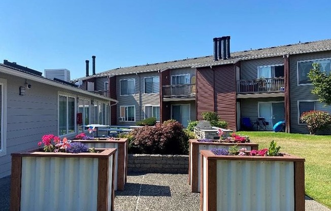 A row of four wooden planters with flowers in front of Pointe East Apartments with patios and balconies.