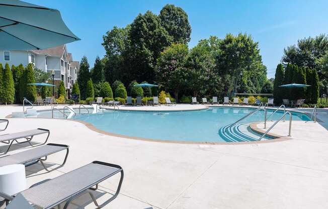 A swimming pool surrounded by trees and lounge chairs.