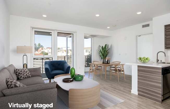 A modern living room with a grey couch, a blue chair, a round coffee table, and a kitchen area in the background.