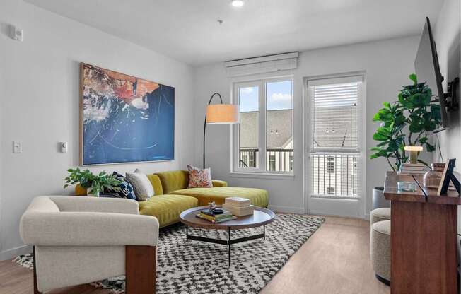 A living room with a yellow couch and a large painting on the wall.