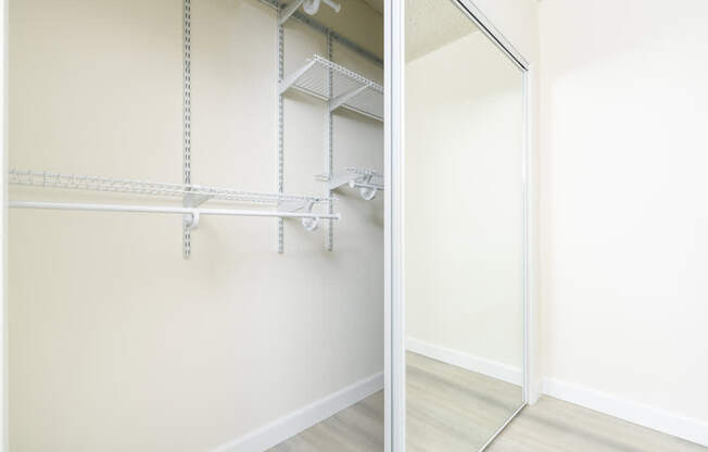 two views of a mirrored closet in a bedroom with white walls and wood floors