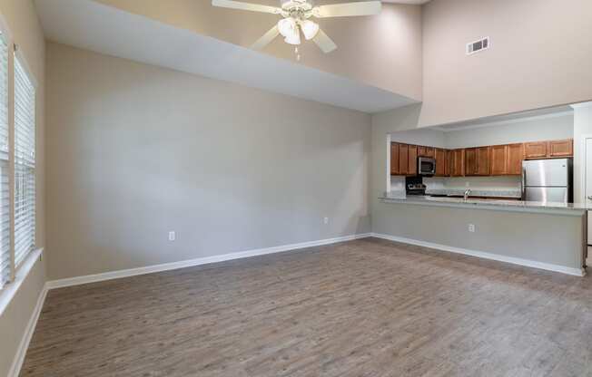 an empty living room with a ceiling fan and a kitchen