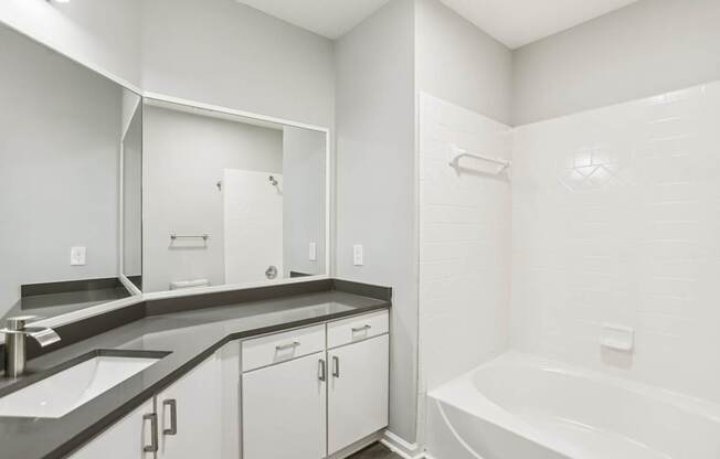 A white bathroom with a sink, mirror, and bathtub.