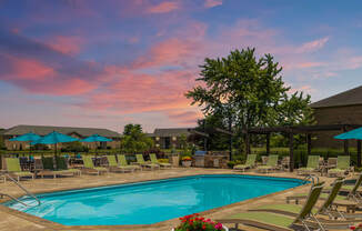 2-Bedroom Apartments in Canal Winchester, OH - The Coleman - Swimming Pool with Chaise Lounge Chairs and Umbrellas by a Brick Building