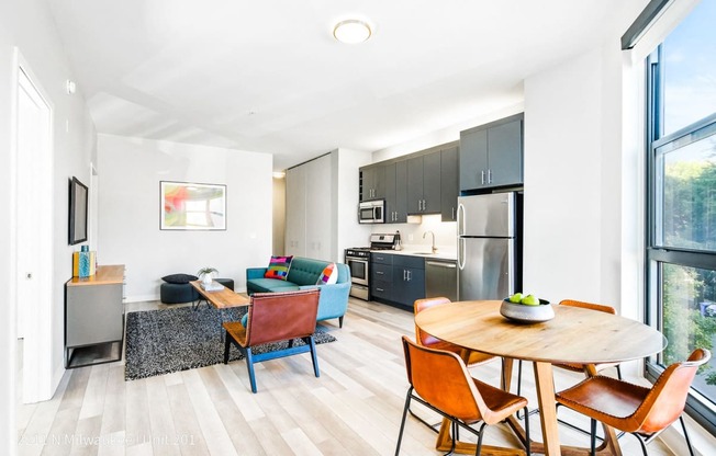 a living room with a table and chairs and a kitchen with stainless steel appliances