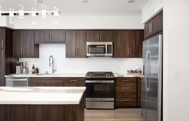 A modern kitchen with dark wood cabinets and stainless steel appliances. at Elements Apartments*, Irvine