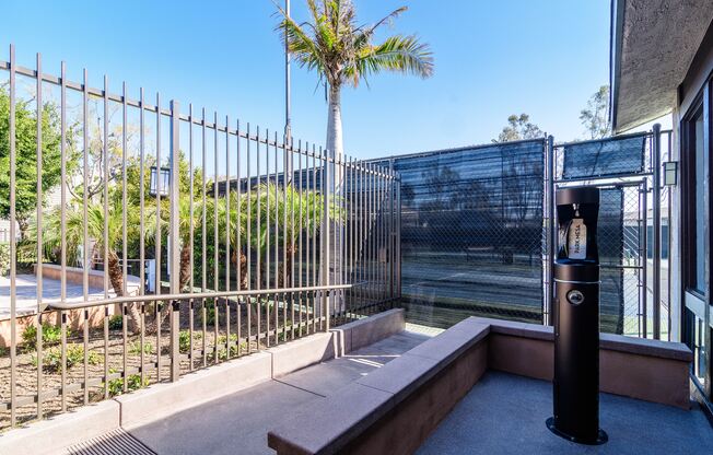 A metal fence with a bench and a trash can in front of a building.