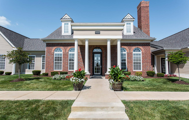 the front of a brick house with white pillars and a sidewalk in front of it