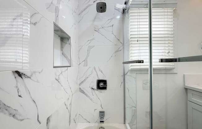 A white bathroom with a marble wall and a glass shower door.