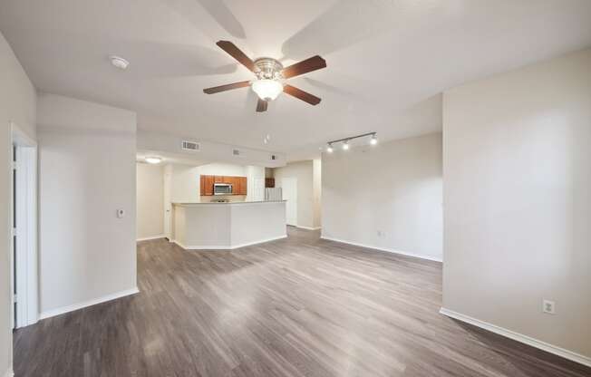 an empty living room with a ceiling fan and a kitchen