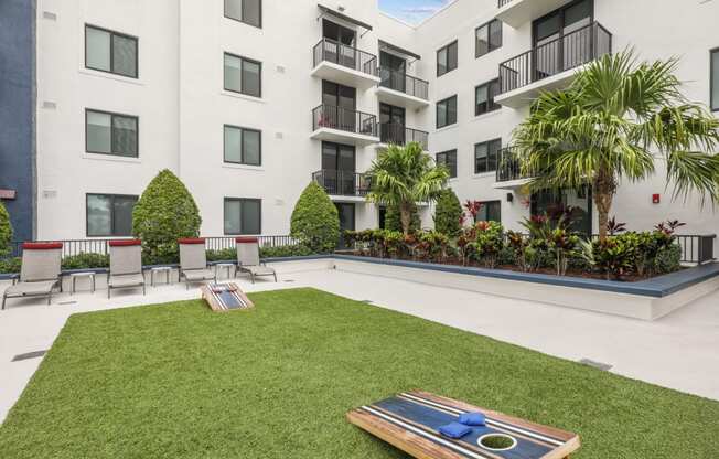 Courtyard area with cornhole boards in green space and chairs at Bay Village 1 in Palmetto Bay, FL