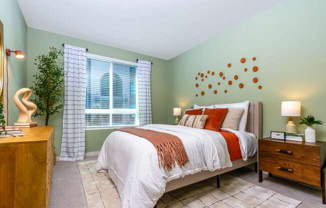 A bedroom with a bed, nightstand, and a window with curtains.