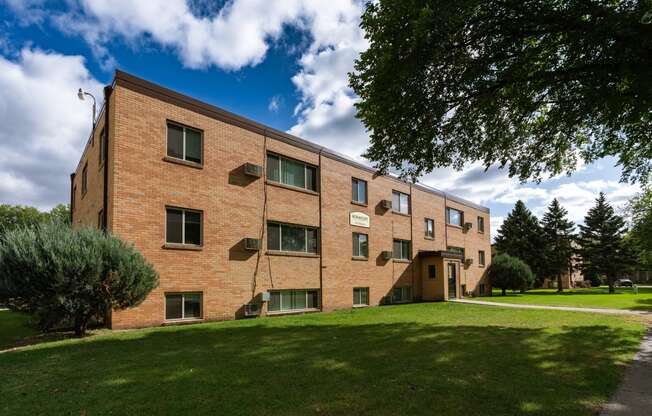 a brick apartment building with green grass and trees. Fargo, ND Morningside Apartments