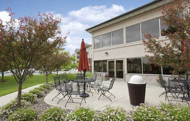 A patio with a table and chairs is surrounded by trees and flowers.