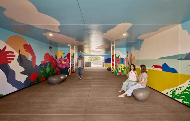 Two women sitting on exercise balls in a room with colorful murals.