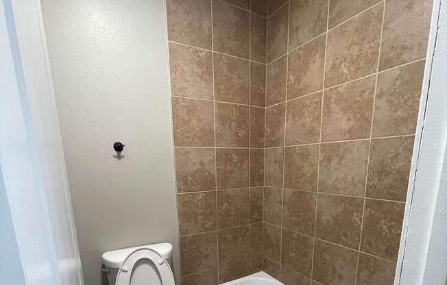 A white toilet with a bidet attachment is installed in a bathroom with beige tiles.