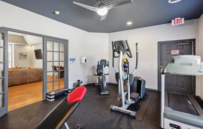 a gym with exercise equipment and a bed in the corner of a room