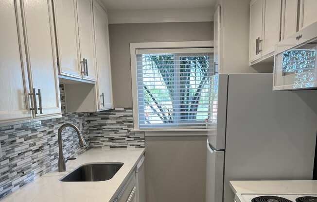 View kitchen with window at end, white cabinets, white countertops, inlaid sink, white appliances, with wood look flooring.