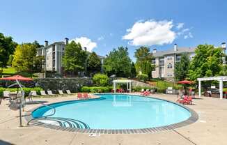 a swimming pool with red chairs and umbrellas and a building in the background