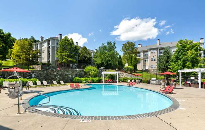 a swimming pool with red chairs and umbrellas and a building in the background