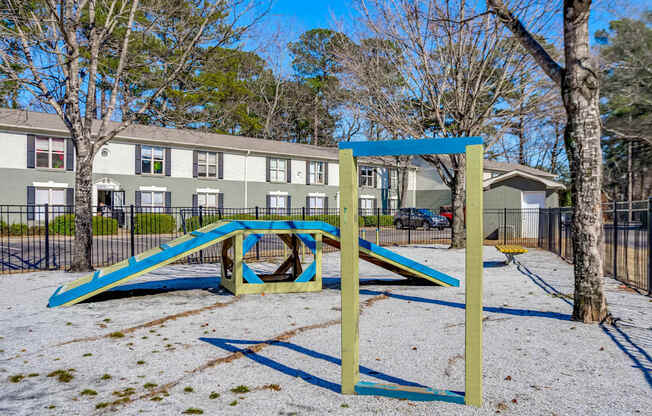 A playground with a blue and yellow slide in the foreground and apartment buildings in the background.