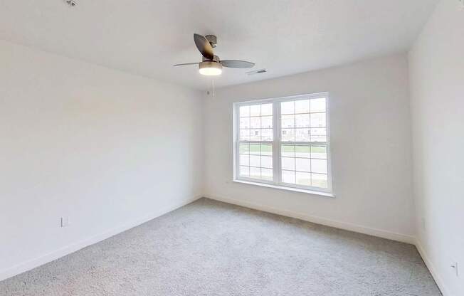 A bedroom with a ceiling fan and a large window at Meadowbrooke Apartment Homes in Kentwood, MI 49512
