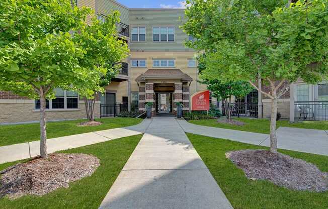 A welcoming exterior entrance here at Swan Creek with landscaped walkway, mature green trees, brick accents, and clear signage, creating a clean, inviting, and well-maintained community setting.