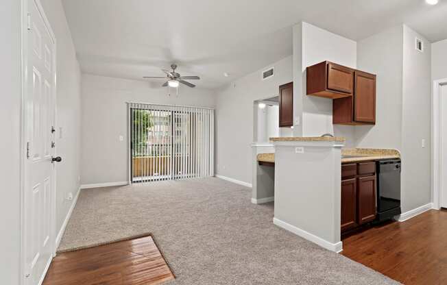 an empty living room with a kitchen and a ceiling fan