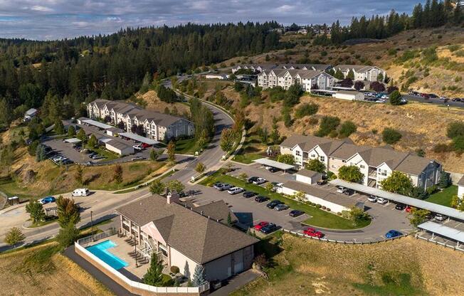 Spokane, WA, Apartments for Rent - Canyon Bluffs - Aerial View of Property Exterior Showing Apartment Buildings, Streets, Parking Lots, Pool Area, Grass Fields, and Trees.