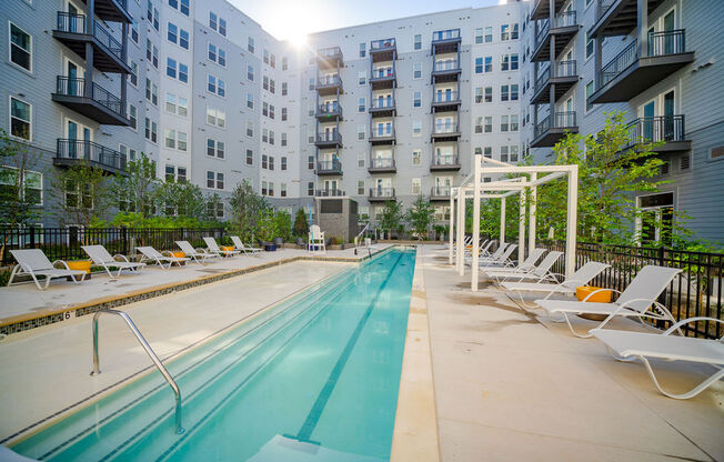 a pool with lounge chairs next to an apartment building