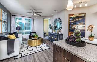 A modern living room with a white sofa, a round gold coffee table, and a large painting on the wall.