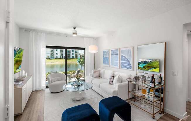 A living room with a white couch, a blue ottoman, and a glass coffee table.