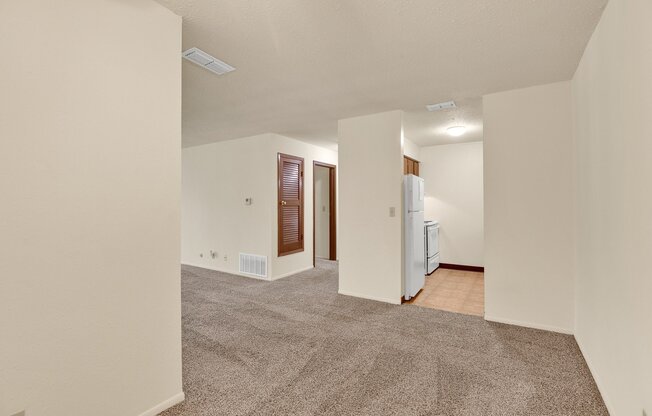 A spacious room with a carpeted floor and a white refrigerator.