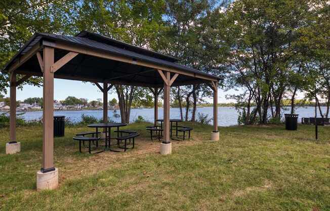 A wooden pavilion with a table and chairs is set up in a grassy area.