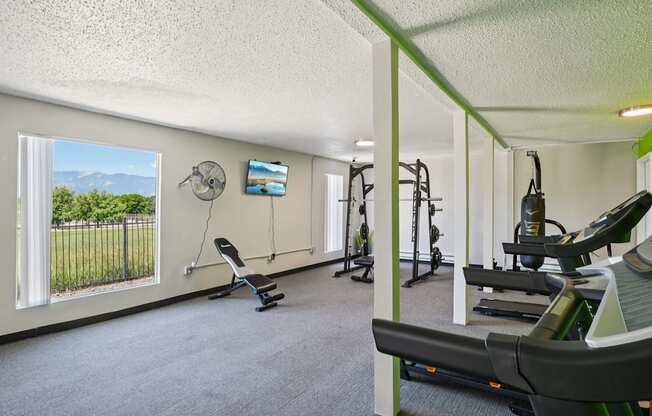 A gym with a row of treadmills and a fan on the wall.