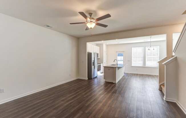 an empty living room with a ceiling fan and a kitchen