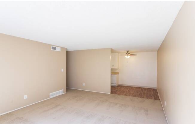 an empty living room with a ceiling fan and a kitchen in the background