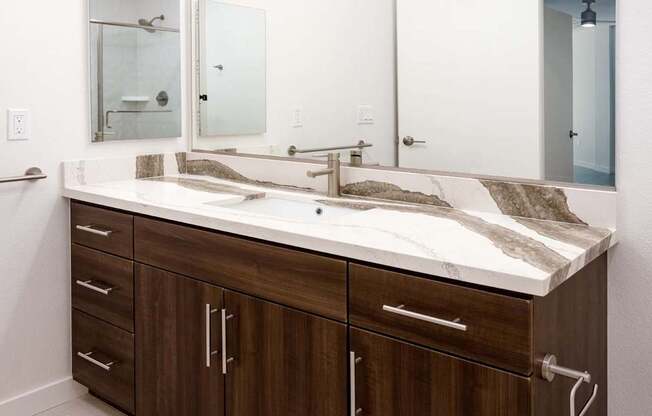 A bathroom with a brown vanity and a white countertop. at Elements Apartments*, Irvine, 92612
