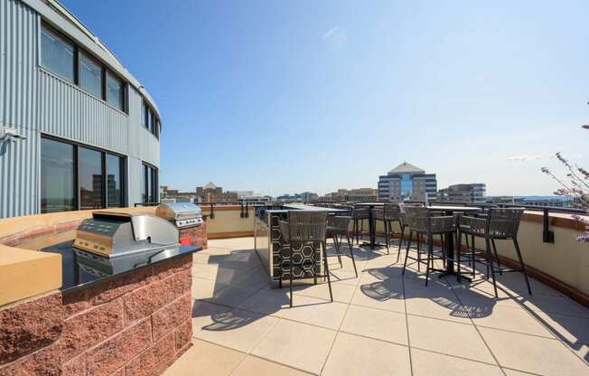 a rooftop patio with tables and chairs and a city in the background