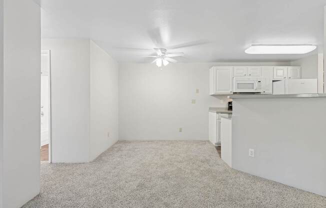 A white room with a ceiling fan and a microwave on top of a cabinet.