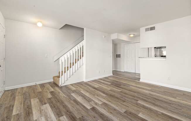 the living room and kitchen of a house with white walls and wood floors