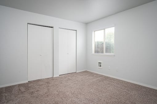 an empty room with white walls and a window and two closets