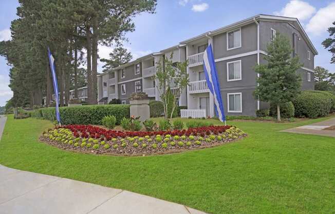 A building with a grey and white exterior is surrounded by a well-manicured lawn and a flower bed.