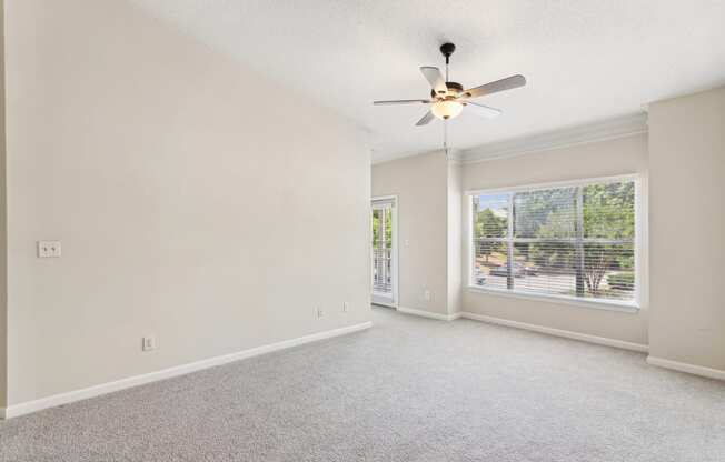 an empty living room with a ceiling fan and a window