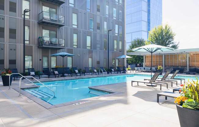A pool area with chairs and umbrellas in front of a building.