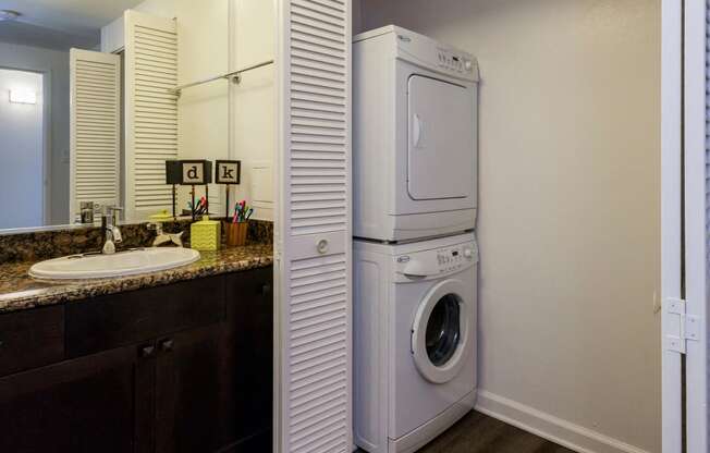 Apartments Palo Alto, CA - Palo Alto Place - Bathroom with Woodstyle Plank Flooring, Dark Cabinets, Vanity Mirror, Granite Countertop, And Laundry Closet With Washer And Dryer.