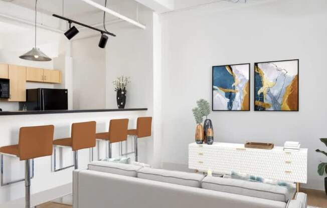 A modern living room with a grey sofa, a bar area with orange chairs, and two abstract paintings on the wall.