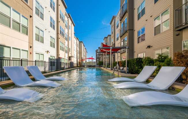 a swimming pool between two apartment buildings with white chairs at Mockingbird Flats, Texas